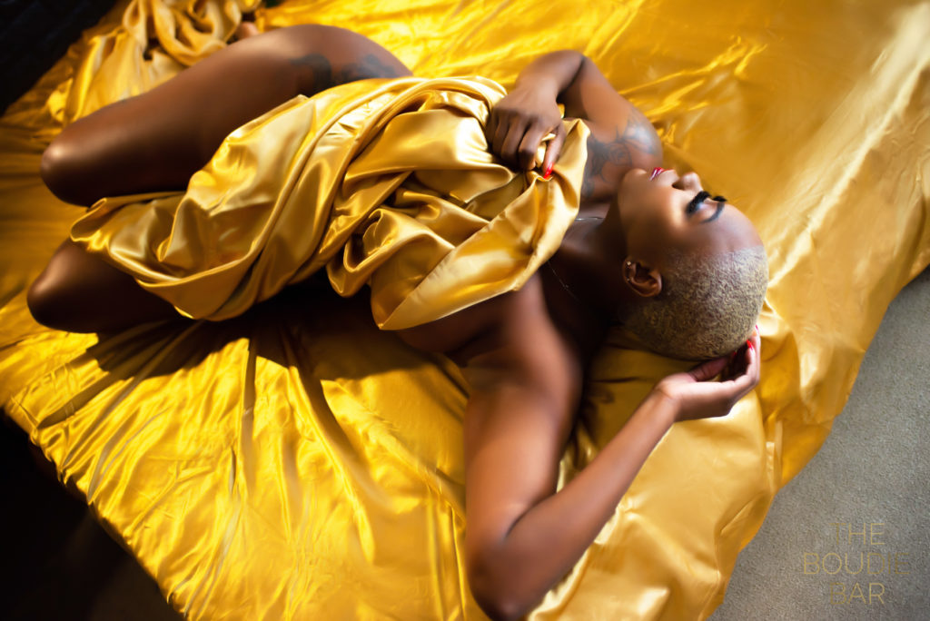 boudoir photo showing a black woman wrapped in a gold satin sheet