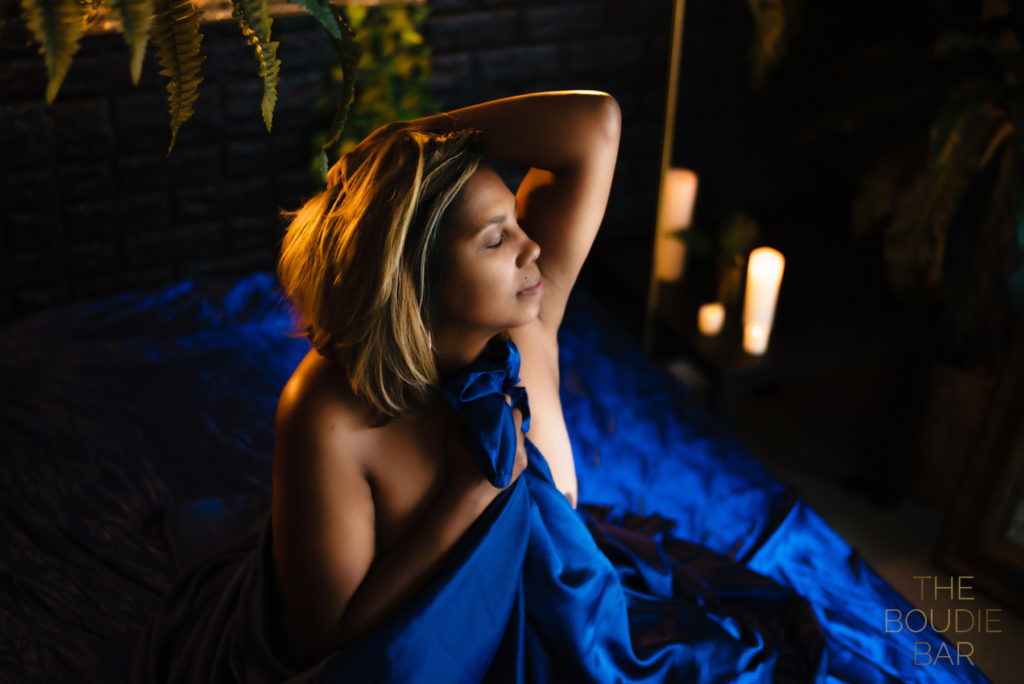 a boudoir photo session showing a black woman wrapped in a blue satin sheet