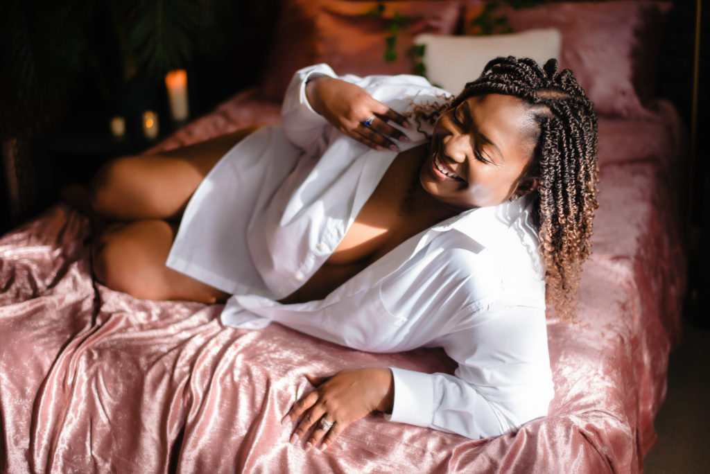 black woman wearing a white button up shirt laying on a bed