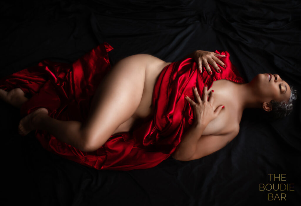 boudoir photo of a beautiful mature woman wrapped in a red satin sheet in a floor pose.