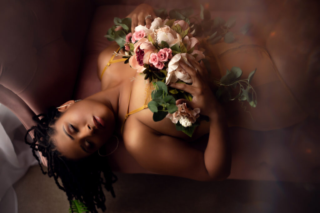 A sensual boudoir image of a black woman using a floral prop.