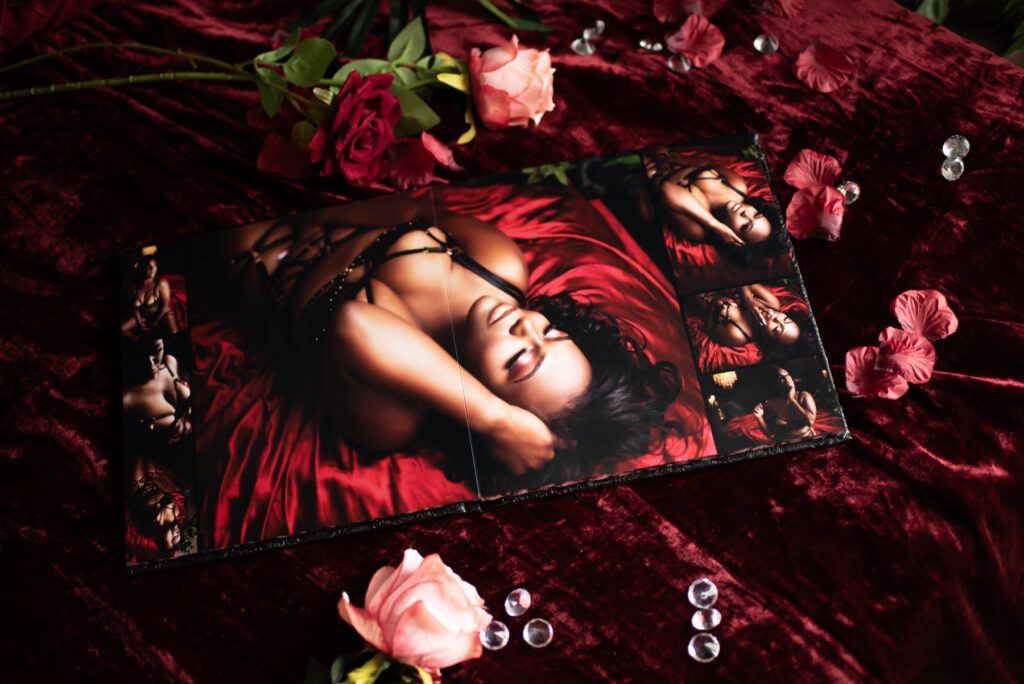 A boudoir photo album sitting open on a bed of roses and red sheets.