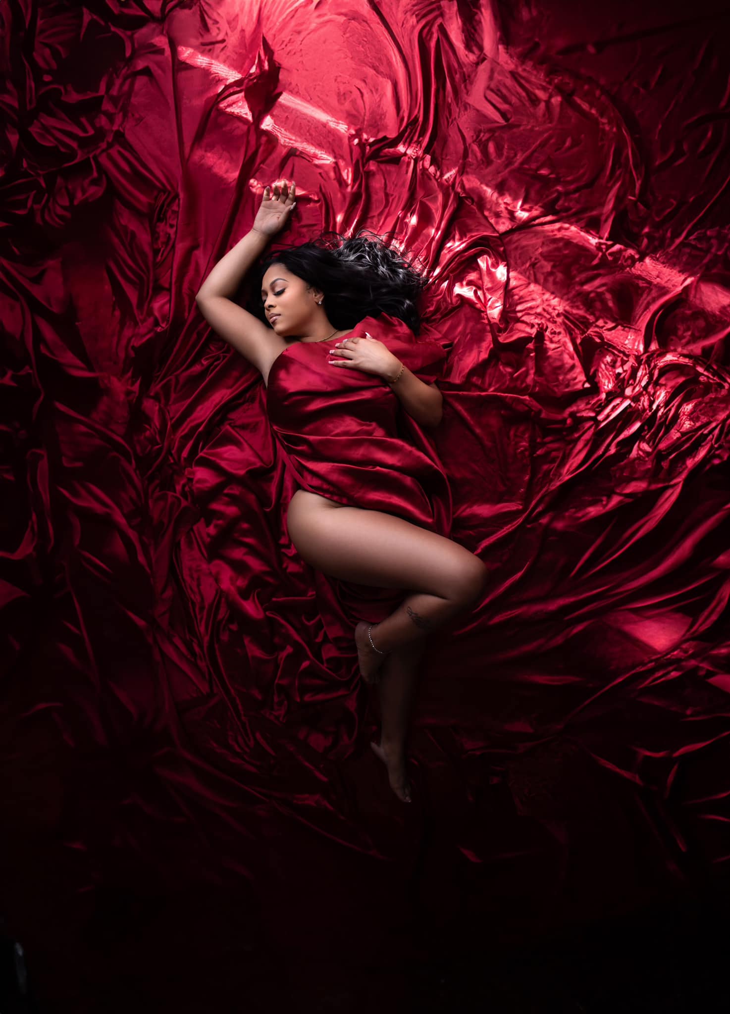 Atlanta boudoir photography featuring a black woman lying on red satin sheets.